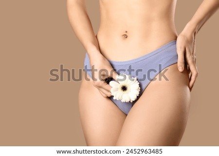 Young woman in panties with beautiful white flower on brown background