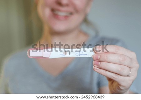 Close up of a happy woman holding a positive pregnancy test, blurred background 