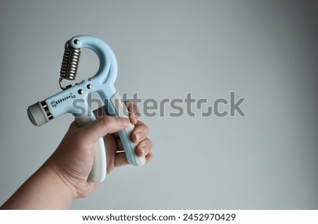 Hand holding light blue and gray colored hand grip exercise tool obect photography isolated on horizontal copy spaced ratio plain light gray background.