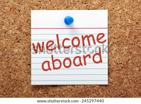 The phrase Welcome Aboard printed on a lined index card and pinned to a cork notice board
