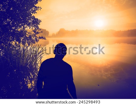 Man watching a sunrise over lake. Human silhouette