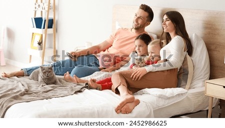 Happy family with cute cats watching TV in bedroom