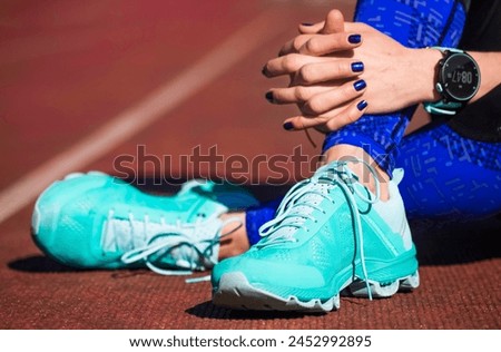 A woman in running shoes. Female in running shoes wearing smart watch rests on a track after the race. Sports and healthy way of life. Healthy lifestyle.