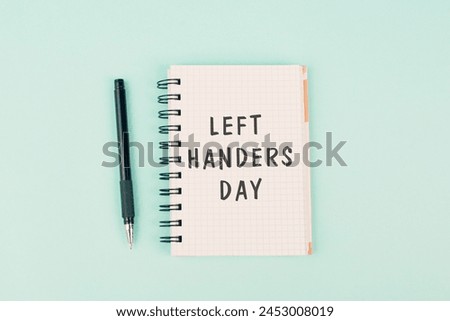 Left handers day is standing on a notebook, writing with the left hand, pen and table Royalty-Free Stock Photo #2453008019