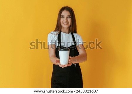 Nice coffee cup. Young woman is against yellow background.