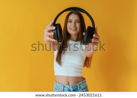 With headphones in hands. Young woman is against yellow background.