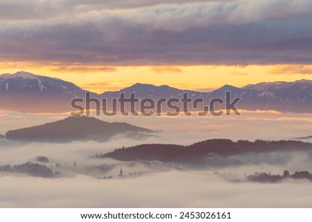 Tiny village of Hörzendorf nestled between the Karawanken mountains, covered in thick fog at sunrise with only a church spire visible, Carinthia, Austria Royalty-Free Stock Photo #2453026161