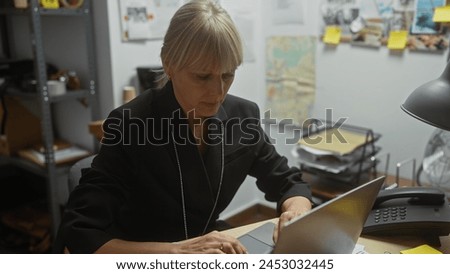 Focused woman detective working on a laptop in a cluttered police department office, evidence board in the background.