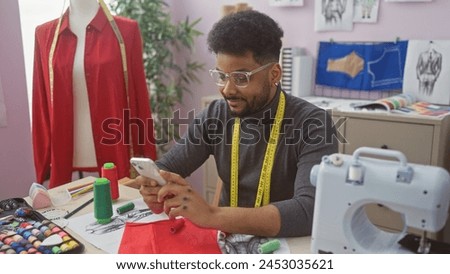 African man in tailor shop using smartphone amid sewing equipment and garments, radiating professionalism.