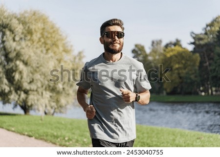 A runner with a beard and sunglasses jogs along a lakeside path, exuding confidence under the bright, open sky.

 Royalty-Free Stock Photo #2453040755