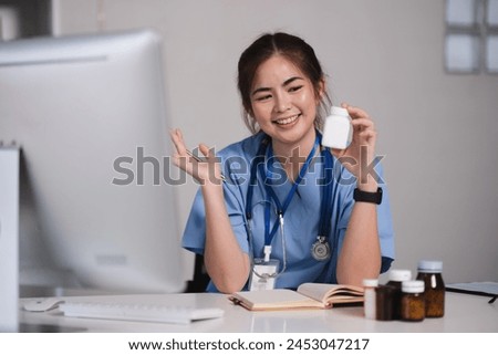 A woman in a blue scrubs is smiling and holding a pill bottle