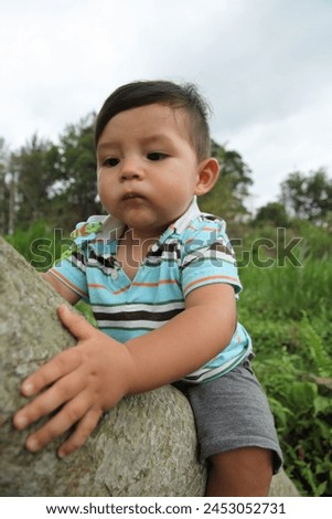 Hong Kong, Asia - 05 03 2011 : Exterior photo view of a cute adorable handsome 1 year old cute good looking baby toddler kid child infant children make boy climbing a tree trunk in a park garden 