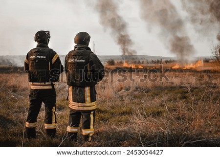 Two Ukrainian firefighters.Spring forest fires are raging. Burning dry grass, reeds in the field.The grass is burning in the meadow.Ecological catastrophy.translat:State Emergency Service of Ukraine
