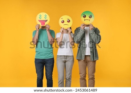 People covering faces with emoticons on yellow background