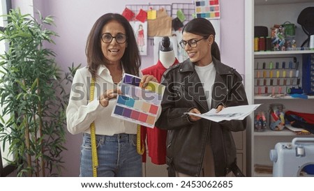 Two women collaborating in a tailor shop, examining fabric colors and fashion designs indoors.