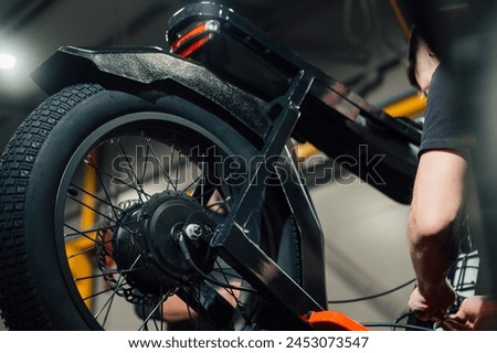 Closeup view of new motorcycle rear wheel in the workshop with pair of workers. Man connects wires at the electro motorbike Royalty-Free Stock Photo #2453073547