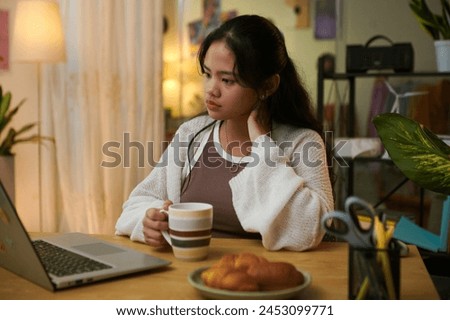 Pensive girl rubbing stiff neck when reading article on laptop screen
