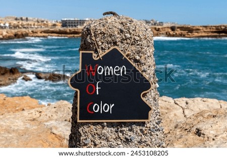 WOC women of color symbol. Concept words WOC women of color on beautiful yellow blackboard. Beautiful stone blue sky sea background. Business WOC women of color social issues concept. Copy space. Royalty-Free Stock Photo #2453108205