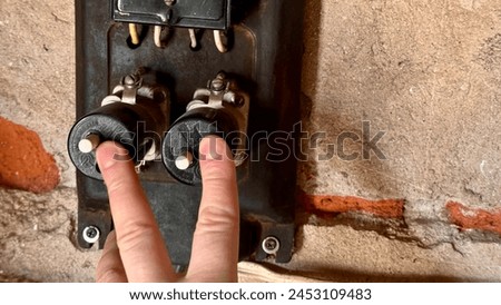 An antique household electricity meter with push-button type electric fuses in the garage. The man's fingers turn off the fuses. Close-up