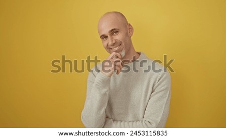A handsome bald man with a beard smiles gently against a yellow background, exuding warmth and friendliness.