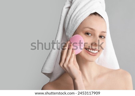 Washing face. Young woman with cleansing brush on grey background, space for text