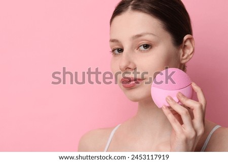 Washing face. Young woman with cleansing brush on pink background, space for text