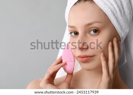 Washing face. Young woman with cleansing brush on grey background, closeup. Space for text