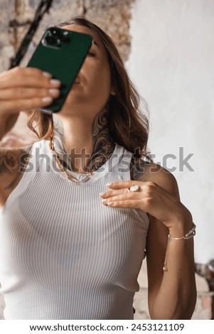 A woman is standing outdoors, holding a smartphone up in front of her to take a picture. She is focused on the screen
