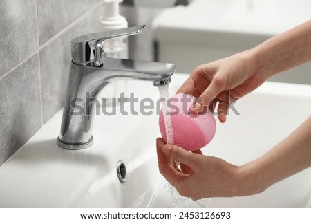 Young woman washing facial brush in bathroom, closeup
