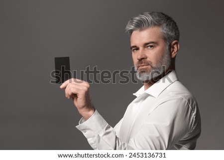 Handsome man holding blank business card on grey background