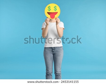 Woman covering face with dollar signs instead of eyes on light blue background