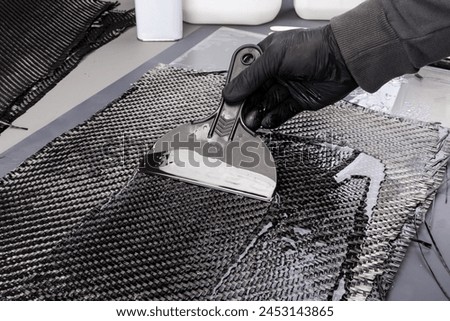 hand working epoxy resin into woven carbon fiber reinforcement cloth. Production manufacturing of a hand laminating CFK composite sheet material.