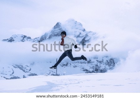 an asian man jumping happily in the middle of the snowy mountains