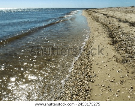 Sea waves are rolling onto the beach of an empty summer beach covered with small stones