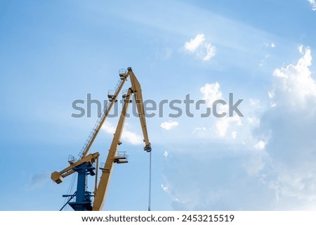 Industrial cranes reach up to a sunlit sky with billowing clouds, a stark contrast of man made machinery and the grandeur of nature, suitable for infratructure projects. High quality photo
