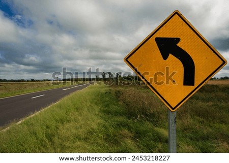 Curved road sign, yellow sign next to cloudy sky