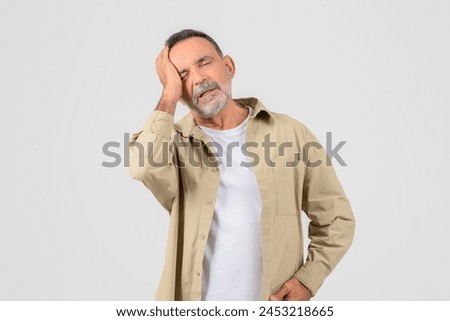 An elderly man holds his head, depicting a stressful or painful moment, isolated on white, have migraine Royalty-Free Stock Photo #2453218665