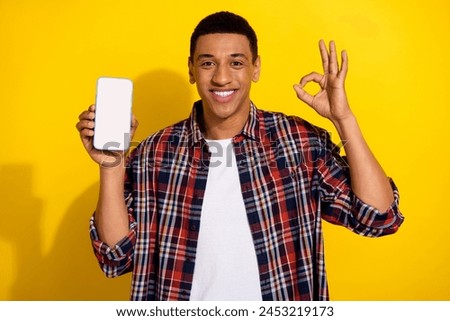 Portrait of satisfied nice guy wear checkered shirt show smartphone screen empty space okey approve isolated on vivid color background