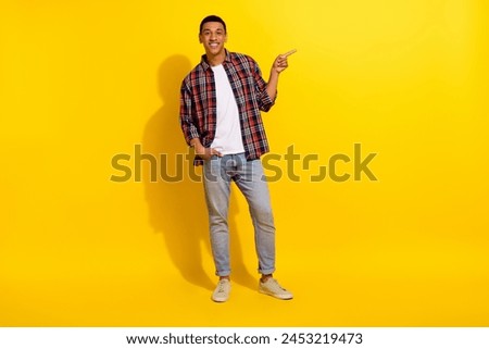 Full length photo of good mood guy wear checkered shirt denim pants indicating at sale empty space isolated on vivid color background