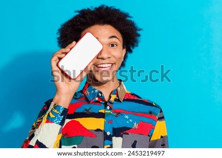 Photo portrait of handsome young guy hold gadget show screen cover eye dressed stylish print garment isolated on blue color background