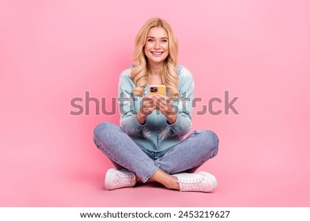 Full size photo of lovely young woman floor crossed legs hold device dressed stylish flower print garment isolated on pink color background