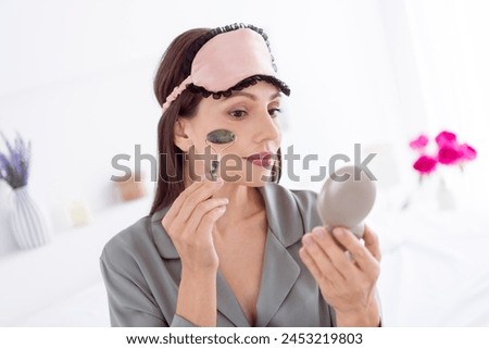 Photo of sweet pretty lady wear grey nightwear looking mirror doing face massage indoors apartment bedroom