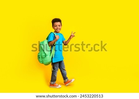 Full body photo of multiethnic multinational child dressed blue t-shirt jeans hold bag showing v-sign isolated on yellow background Royalty-Free Stock Photo #2453220513