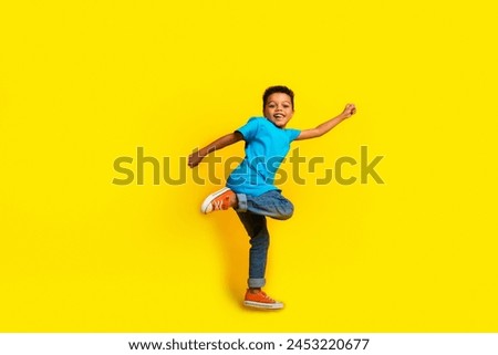 Full size photo of multiethnic multinational little schoolboy wear blue t-shirt denim pants fly arm up isolated on vivid yellow background Royalty-Free Stock Photo #2453220677