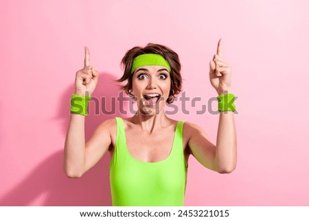 Photo of funny excited lady dressed green sportive bodysuit pointing two fingers up empty space isolated pink color background