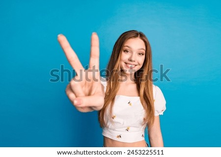 Photo of happy positive girl make v sign in camera isolated blue color background