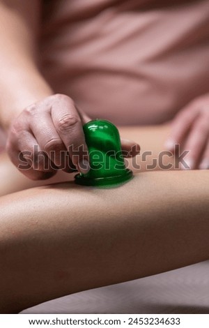 A massage therapist does a lymphatic drainage massage of the calf muscles with a vacuum plastic jar. Vertical photo.
