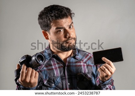 Young man indecisive between a camera and the camera of his mobile phone. Man deciding whether to use a professional camera or a mobile camera. Comparing cameras