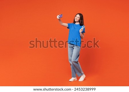 Full body young smiling happy woman she wear blue t-shirt casual clothes doing selfie shot on mobile cell phone post photo on social network isolated on plain red orange background. Lifestyle concept