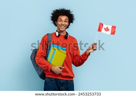 A happy black guy showing vibrant energy and international awareness by waving the Canadian flag beside bright textbooks, all against a clear, blue isolated background